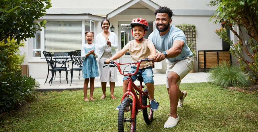 Child learning to ride a bicycle in his backyard with family